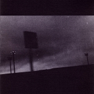 An image at night pointed toward an overcast sky and tinted a deep purple. The silhouette of a road sign in the foreground is blurred as we rush past, presumably in a car. Three large and powerful lamp posts are in the background. The image is grainy and no details can be made out.