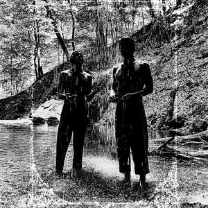 A black and white photograph of two silhouetted figures in a shallow river, underneath a small waterfall. One looks at the camera, holding something in their hands. The other has their arms out to catch the droplets and looking up into the spray. They are wearing pants but not shirts.